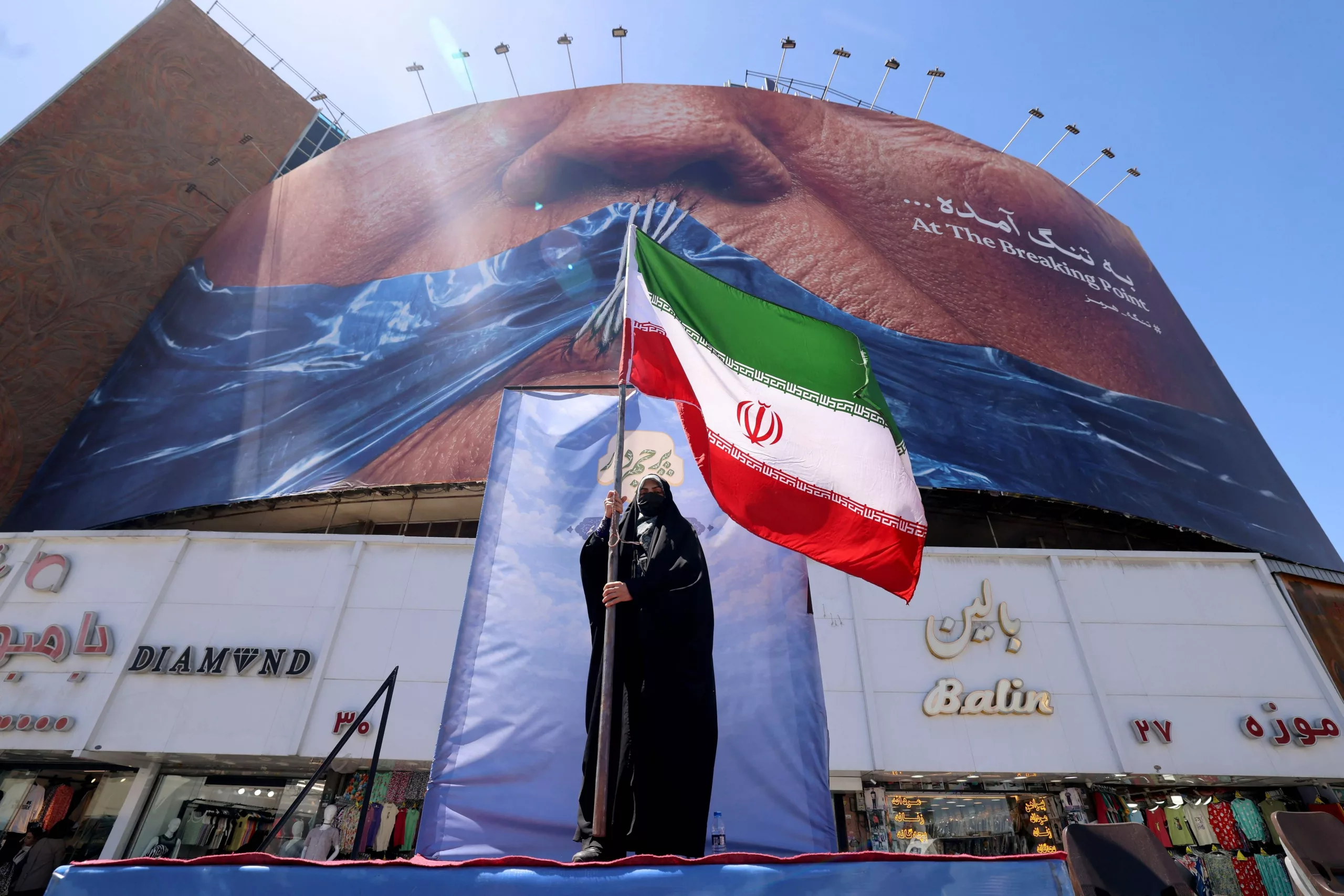 Una mujer sostiene la bandera iraní frente a una valla publicitaria antiestadounidense que hace referencia al presidente Donald Trump