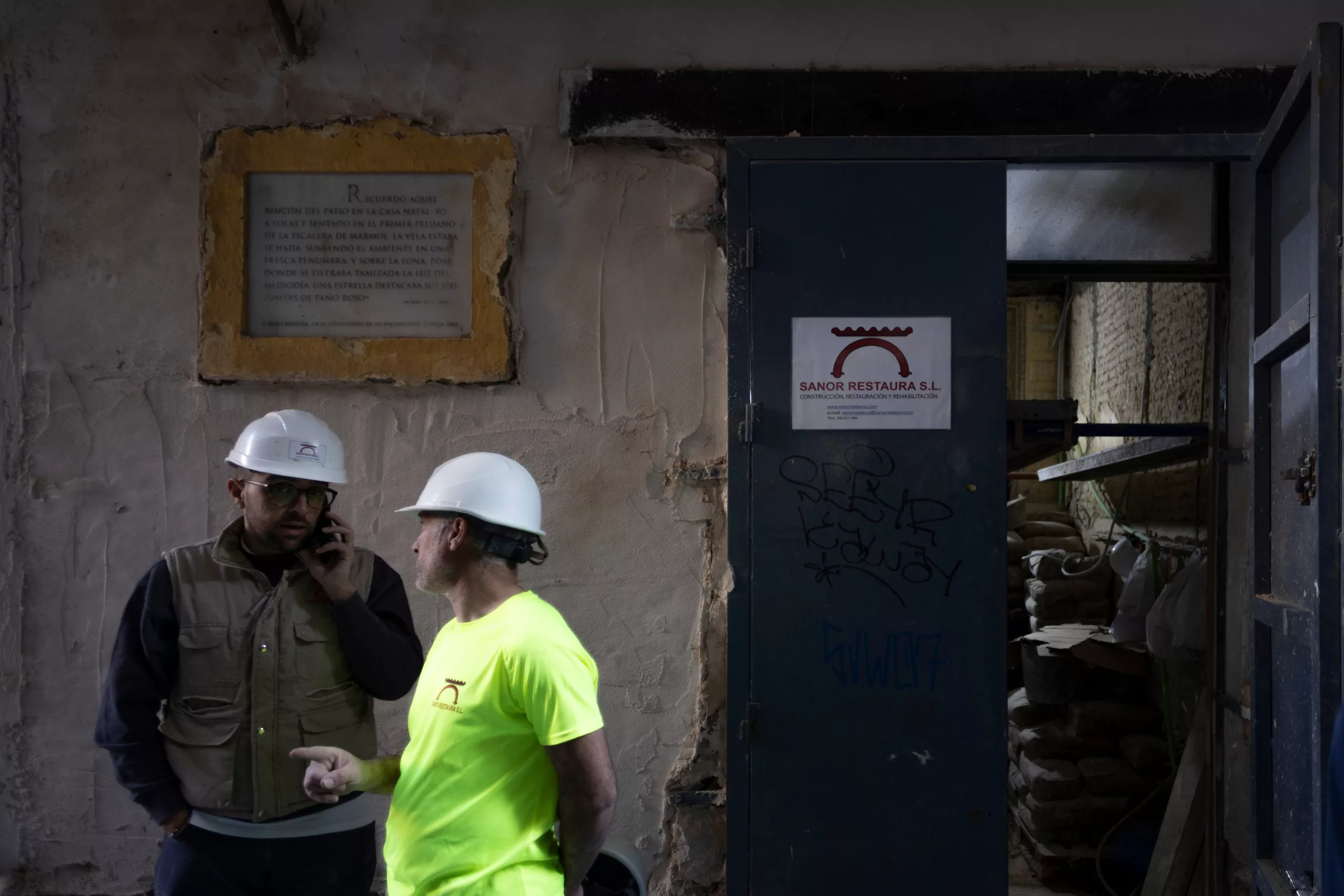 Dos operarios frente a placa informativa en el exterior de la vivienda indicando que fue la casa de Luis Cernuda.