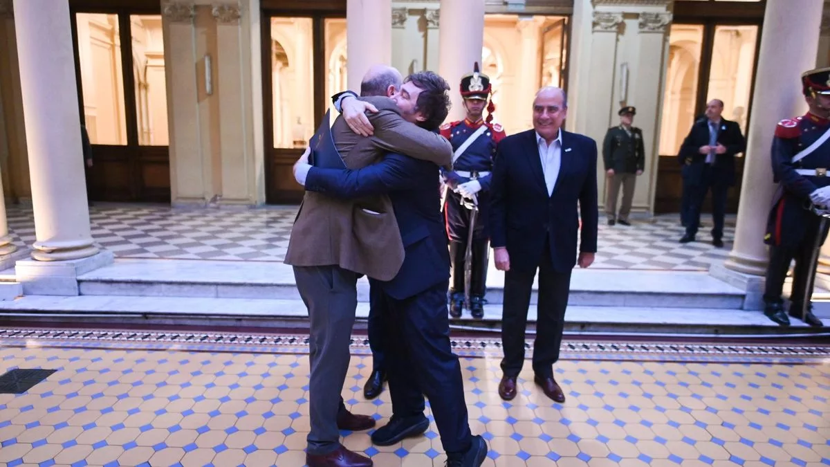 Javier Milei y Federico Sturzenegger se funden en un abrazo, ante la mirada de Guillermo Francos.
